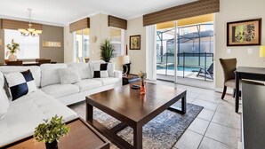 Ein geräumiges Wohnzimmer mit einer großen Couch, einem Couchtisch und Blick auf einen Balkon mit einem Pool.