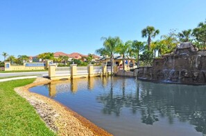 A water feature with a bridge, palm trees, and houses in the background.