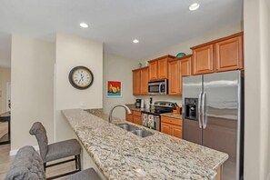 A kitchen with granite countertops, wooden cabinets, stainless steel appliances, and a clock on the wall.