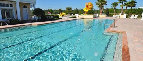 A swimming pool with clear blue water, surrounded by lounge chairs and palm trees.