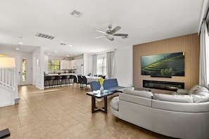 A modern living room with a sofa, a coffee table, a TV, and a dining area with chairs and a table.