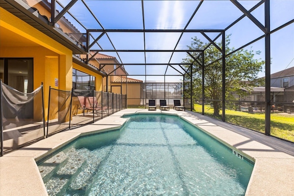 A swimming pool with a glass enclosure, surrounded by a fence and chairs, with a clear view of the surrounding area.