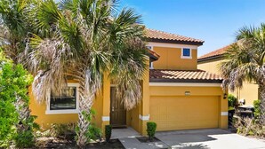 A yellow house with a garage, surrounded by palm trees and a small garden. - South Pool | Waterslide | Golf | Near Disney 2609 (Davenport)