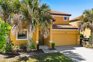 A yellow house with a garage, surrounded by palm trees and a small garden. - South Pool | Waterslide | Golf | Near Disney 2609 (Davenport)