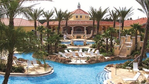 Ein Resort mit einem zentral gelegenen Pool, Palmen und einem Gebäude mit rotem Ziegeldach.
