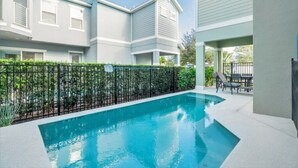 A swimming pool with a black fence, surrounded by a building with a light blue exterior and white trim. - Private Pool | 15 Min to Disney | Gated Resort 1472 (Kissimmee)