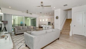 A modern living room with a large white sofa, a coffee table, and a dining area with a kitchen in the background. - Private Pool | 15 Min to Disney | Gated Resort 1472 (Kissimmee)