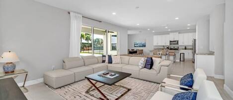 A modern living room with a sectional sofa, a coffee table, and a view of the kitchen in the background.