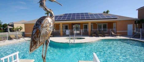 A swimming pool with a bird sculpture in the center, surrounded by lounge chairs and a building with solar panels.