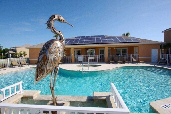 A swimming pool with a bird sculpture in the center, surrounded by lounge chairs and a building with solar panels.