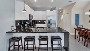 Une cuisine moderne dotée d’un grand îlot central, de tabourets de bar, d’appareils électroménagers en acier inoxydable et de luminaires suspendus.