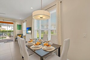 Enjoy meals in this stylish dining area with a table for four, featuring a ceiling light fixture and large windows with blinds.