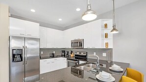 Eine moderne Küche mit Edelstahlgeräten, weißen Schränken und Granitwerkplatten sowie einem gelben Stuhl.
