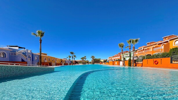 A clear blue pool surrounded by colorful buildings with palm trees. - VF012 Apartament LaBella Cumbre del Sol - Benitachell, Costa Blanca (Benitachell)