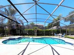 Une piscine dotée d’une structure en verre, entourée d’une haie et de palmiers.