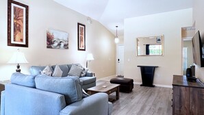 Ein Wohnzimmer mit einer Couch, einem Couchtisch, einer TV-Konsole und gerahmten Kunstwerken an den Wänden.