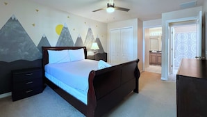 Ein Schlafzimmer mit Bett, Nachttisch, Kommode, Deckenventilator und Wandgestaltung mit Bergmotiv.