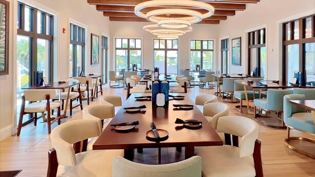 A spacious dining area with long tables, chairs, and large windows offering views of palm trees. - South Pool | Game Room | 7 Miles to Disney 1504 (Kissimmee)