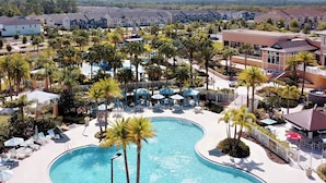 A resort with a large, curved swimming pool surrounded by palm trees and lounge chairs. - South Pool | Game Room | 7 Miles to Disney 1504 (Kissimmee)