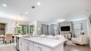 A modern kitchen with a large island, white cabinetry, and a dining area with a table and chairs. - South Pool | Game Room | 7 Miles to Disney 1504 (Kissimmee)