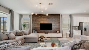 Uma sala de estar moderna com um sofá modular, uma mesa de centro de vidro e uma TV de tela plana fixada em uma parede de madeira.