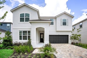A two-story house with a garage, a front entrance with a small porch, and a landscaped front yard. - Star Wars Game Room • Mickey & Harry Potter • Pool & Spa • Gated Near Disney (Kissimmee)