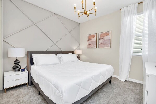 A bedroom with a bed, nightstands, a chandelier, and artwork on the wall.