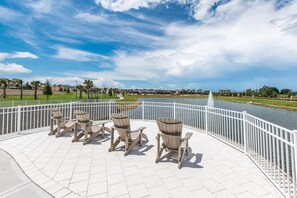 Relax in comfort with Adirondack chairs surrounding a central table on a paved deck overlooking a serene body of water.