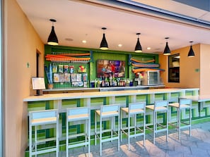 Una zona de bar con mostrador, varias luces colgantes y una fila de taburetes.