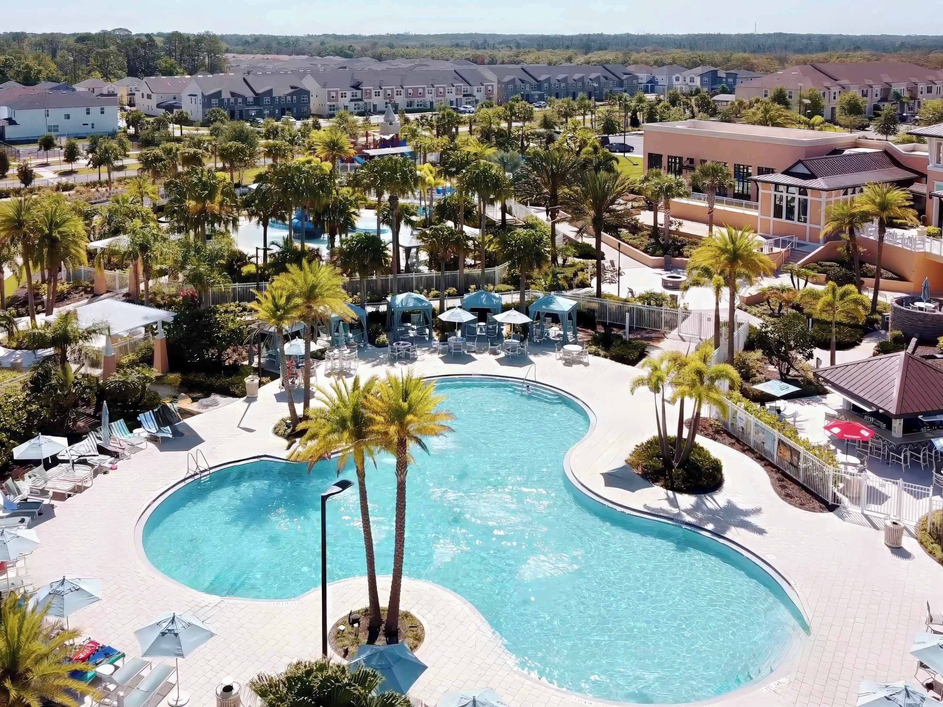 A resort with a large, curved swimming pool surrounded by palm trees and lounge chairs.