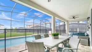 Un patio techado con piscina, muebles de mimbre y vistas a casas vecinas.