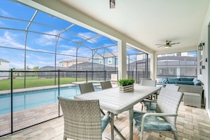 Eine überdachte Terrasse mit Pool, Korbmöbeln und Blick auf Nachbarhäuser.