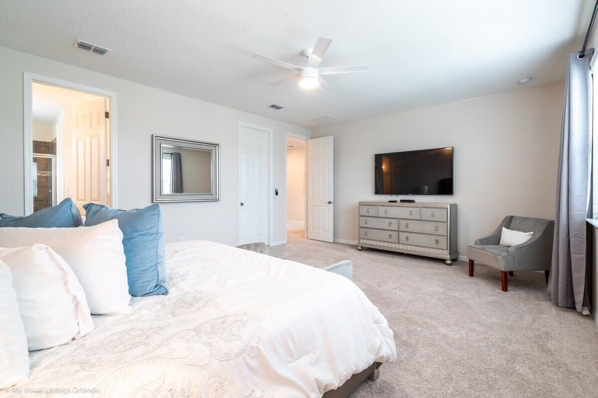 A bedroom with a bed, dresser, TV, and a chair.