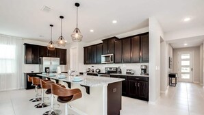 A modern kitchen with dark cabinets, a central island with bar stools, and pendant lighting.