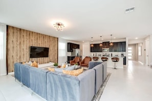 A modern living room with a large sofa, a TV, and a kitchen in the background.