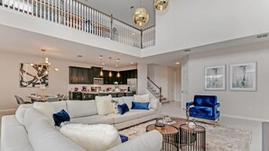 A spacious living area with a large sectional sofa, a coffee table, and a blue armchair. A kitchen is visible in the background. - Harry Potter | Harley Game Loft | Near Disney 1787 (Kissimmee)
