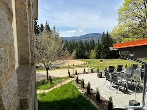 Un patio con mobiliario exterior, vistas a un jardín ajardinado y una bandera a lo lejos.