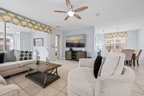 A modern living room with a ceiling fan, a flat-screen TV, and a dining area with a table and chairs.