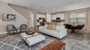 Uma sala de estar espaçosa com um sofá branco, duas poltronas, uma mesa de centro e um espaço de jantar com mesa e cadeiras.
