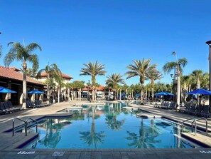 A pool area with lounge chairs and umbrellas, surrounded by palm trees and buildings with red-tiled roofs. - No Rear Neighbors | Resort | Pool | Game Room 4183 (Davenport)