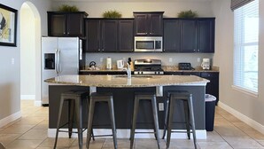 A modern kitchen with dark cabinets, stainless steel appliances, a granite countertop, and three bar stools. - Value Near Disney | Waterslides & Private Pool 4204 (Davenport)