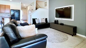 Een moderne woonkamer met een zwarte leren bank, een grijze muur en een flatscreen televisie boven een donkere console tafel.