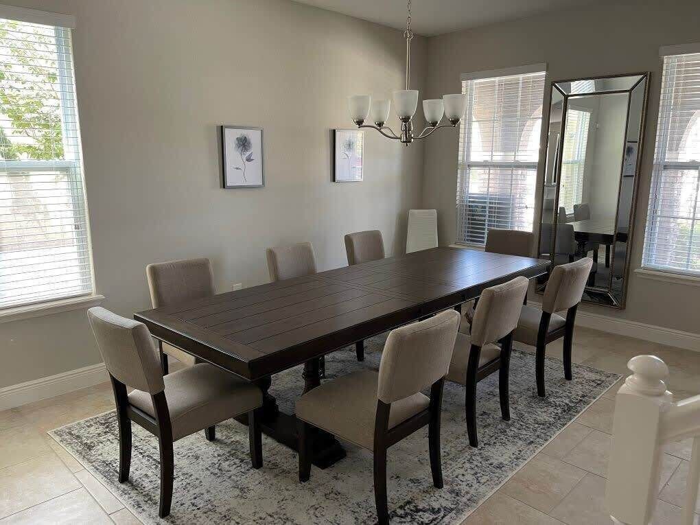 Comedor con una larga mesa de madera, seis sillas, un candelabro y cuadros en las paredes.