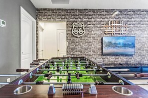 Een tafelvoetbaltafel in een kamer met een bakstenen muur, een televisie en een deur.