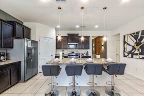 Une cuisine moderne avec des meubles de couleur sombre, un réfrigérateur en acier inoxydable, un four à micro-ondes encastré et un îlot central doté de tabourets de bar.