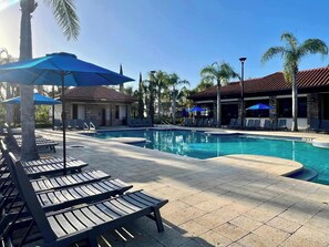 A pool area with lounge chairs, umbrellas, and a building with a tiled roof. - Star Wars | Princess | Mickey | Pool | Disney 7036 (Davenport)