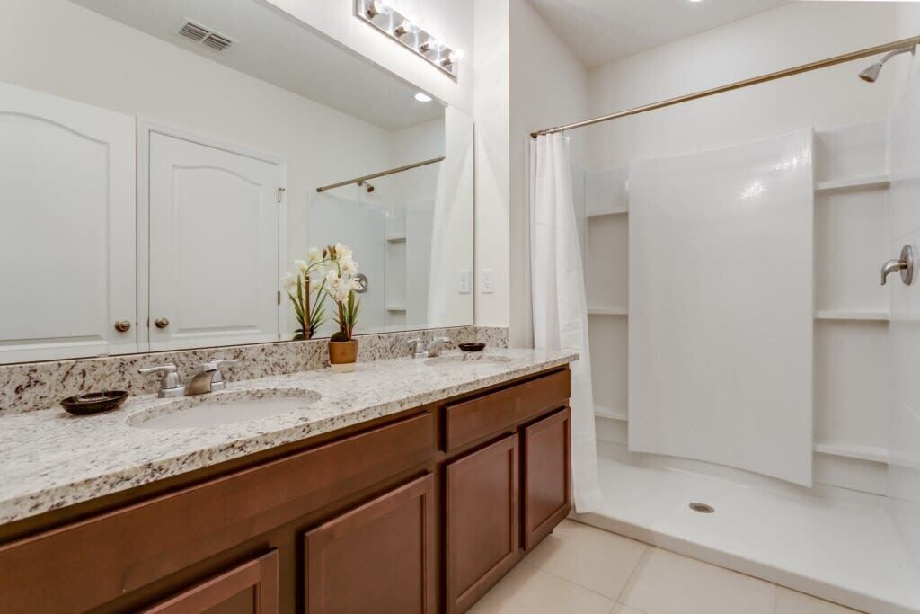 A bathroom with a double sink vanity, a large mirror, a shower with a glass door, and a potted plant.