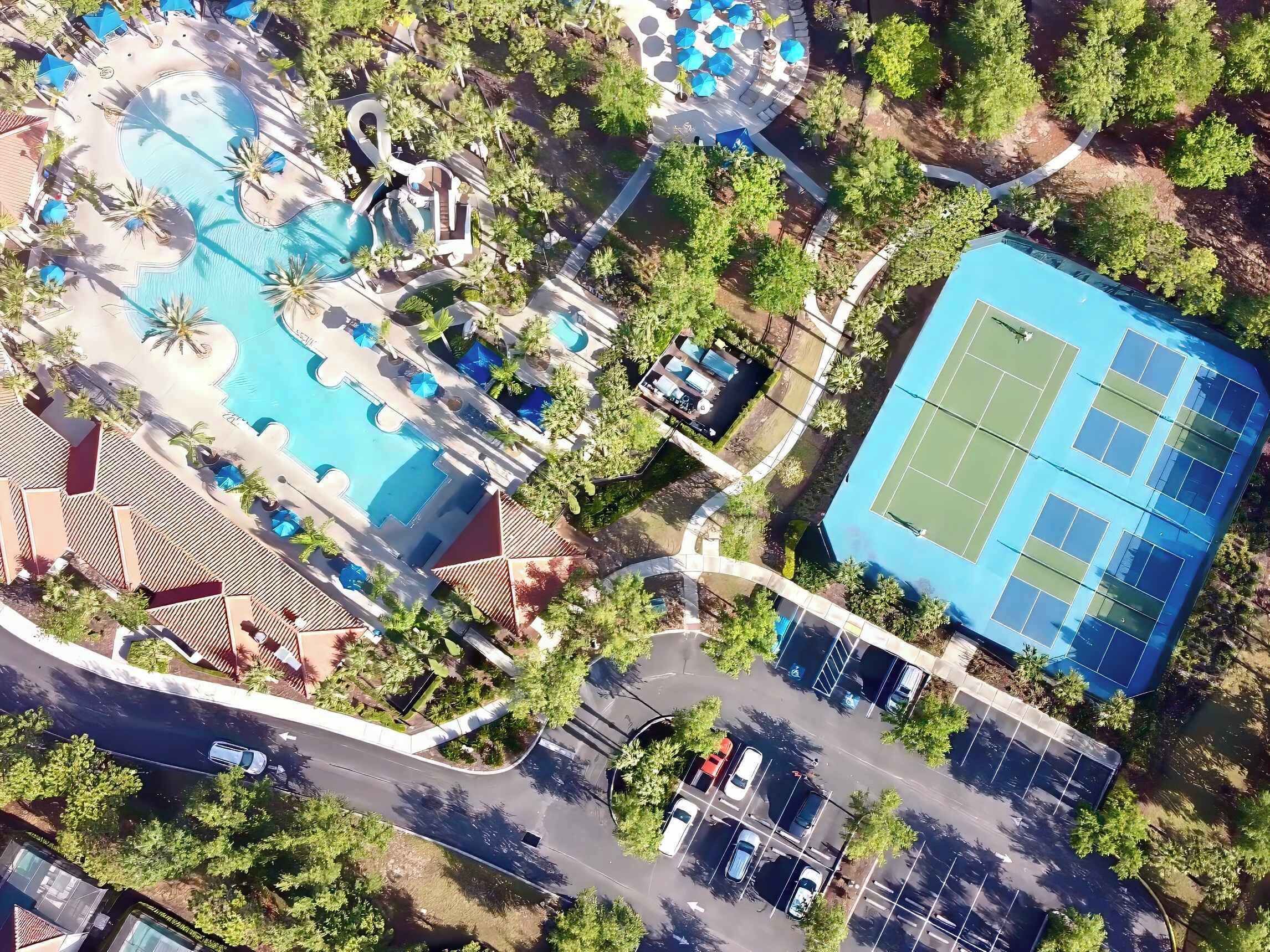 Ilmakuva lomakeskuksesta, jossa on useita uima-altaita, tenniskenttä ja pysäköintialue.
