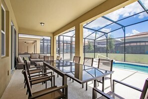 A spacious indoor area with a glass table and chairs, large windows, and a view of a swimming pool.
