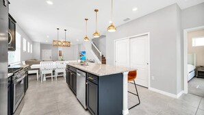 A modern kitchen with a central island, white chairs, and pendant lighting. - Private Pool | Gated Resort | 15 Min to Disney 7299 (Davenport)